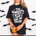 Person wearing a black t-shirt with Halloween-themed text, holding a mug, with bat decorations in the background.