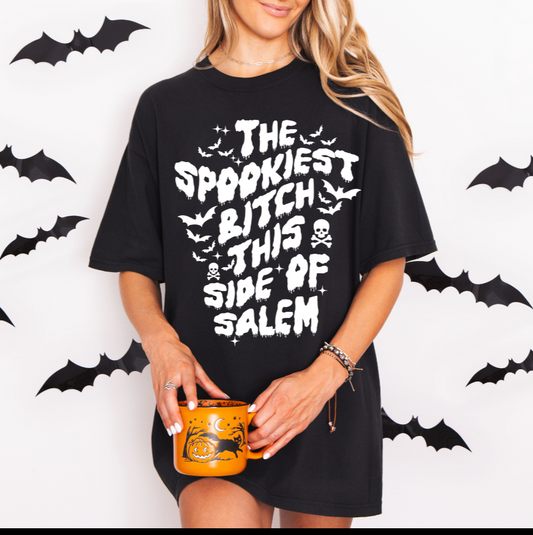 Person wearing a black t-shirt with Halloween-themed text, holding a mug, with bat decorations in the background.